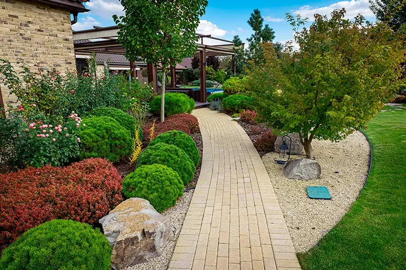 Ścieżka na taras przy domu w otoczeniu kwiatów, zieleni i drzew